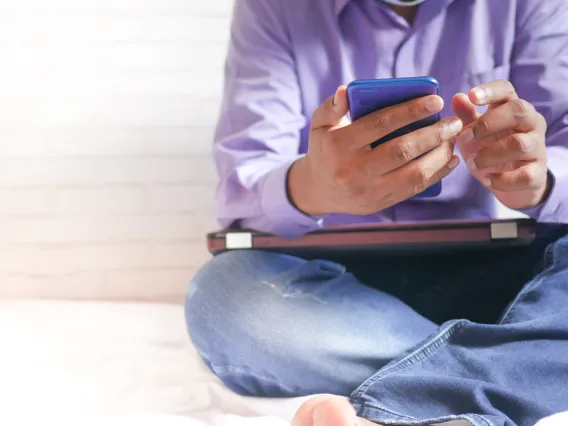 person sitting on a bed holding a smart phone in their hands