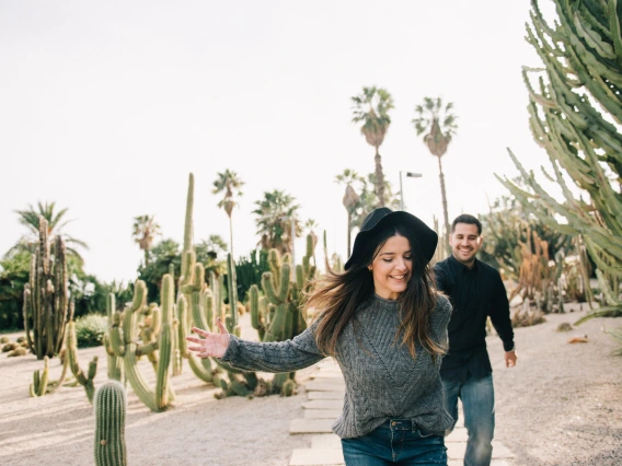 two people walking in the desert with cacti and palm trees in the background