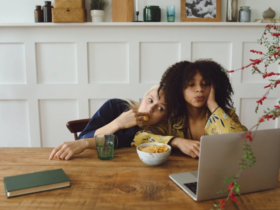 two people eating a snack and watching someone on a laptop