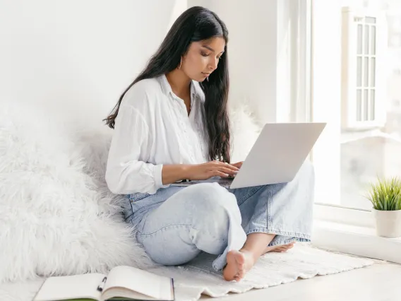 person sitting on a bed typing on a laptop