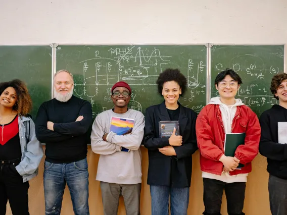 group of students and a professor standing in front of a blackboard and smiling