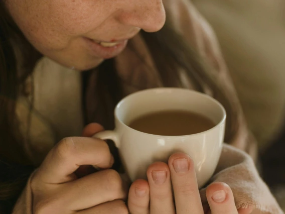 person wrapped in a blanket smelling a cup of coffee