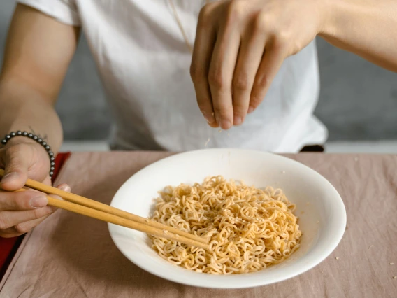 person sprinkling salt onto a bowl of noodles