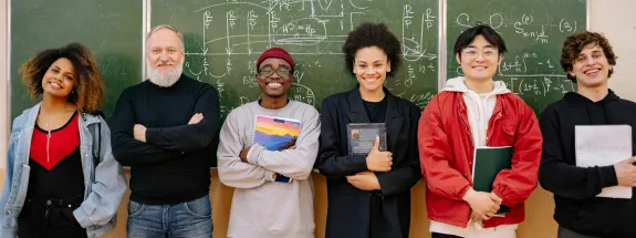 group of students and a professor standing in front of a blackboard and smiling