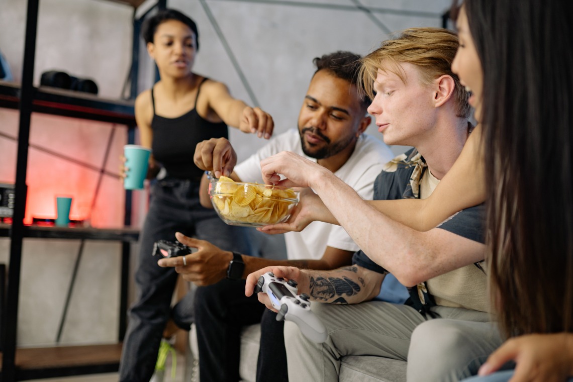 a group of people sitting on a couch playing video games and eating potato chips