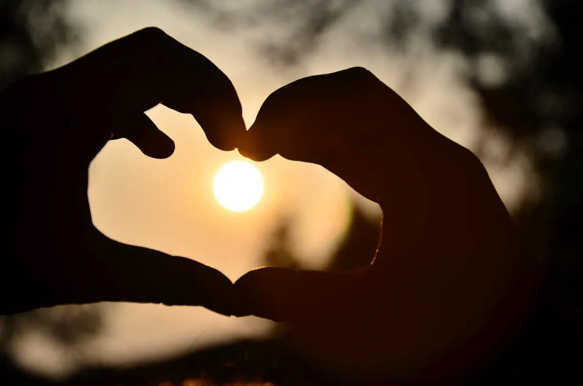 silhouette of hands in a heart shape with the moon in the background