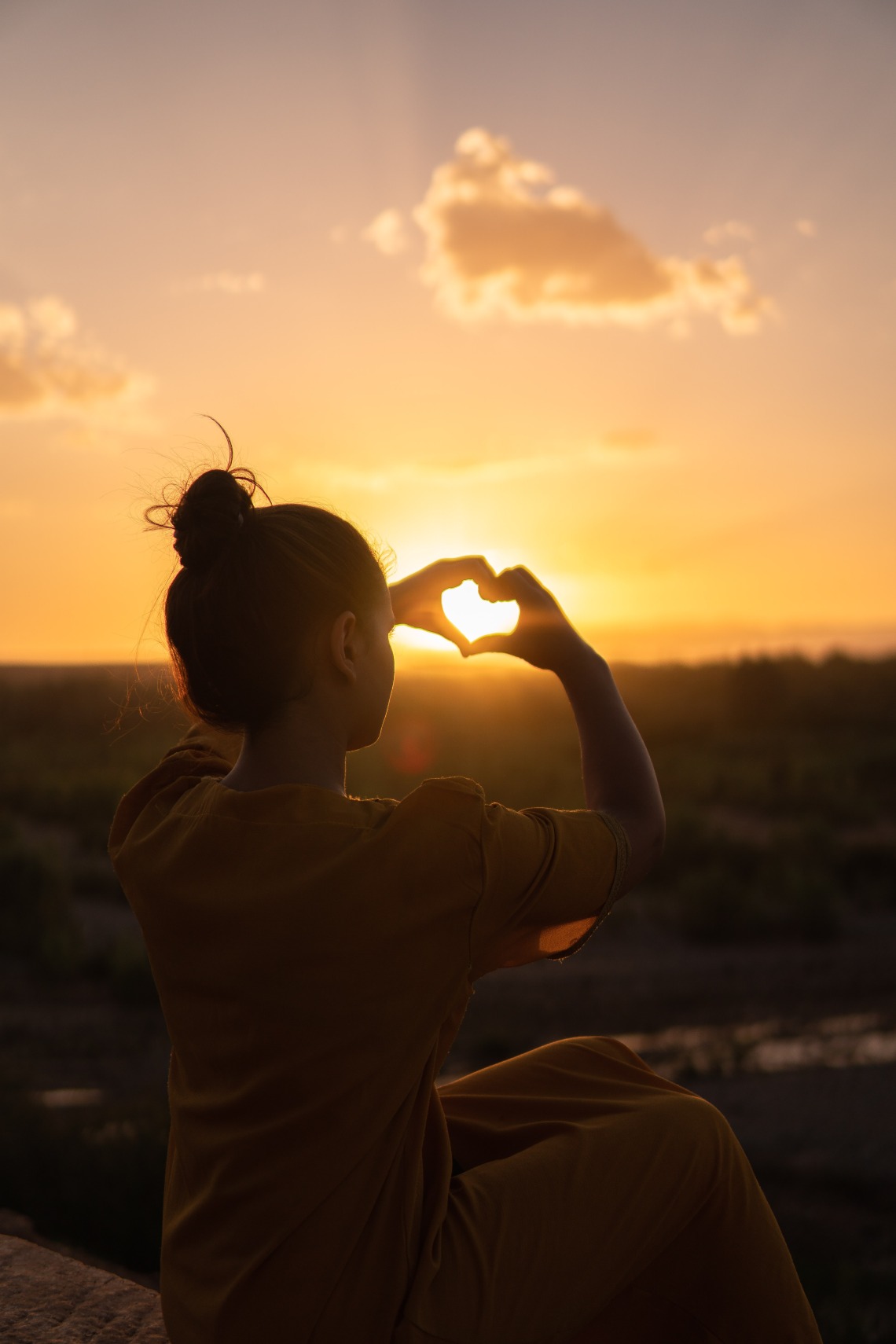 silhouette of hands in a heart shape with a sunset in the background