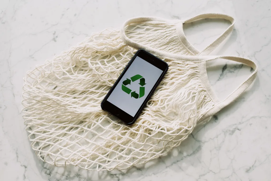 reusable shopping bag and a phone with a recycling symbol shown on the screen