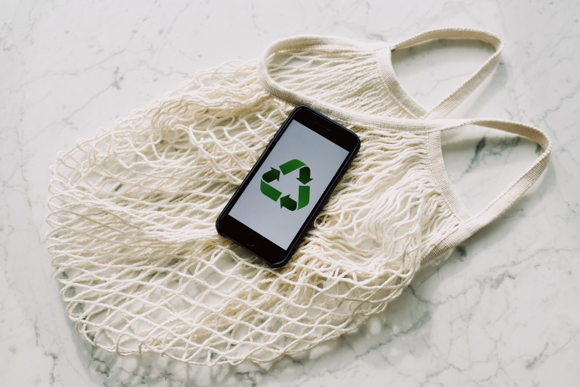 reusable shopping bag and a phone with a recycling symbol shown on the screen