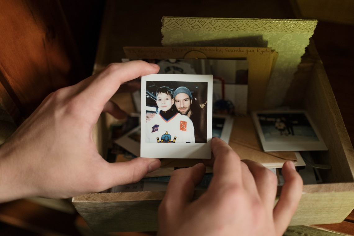 two hands holding a photo with a box of photos and notes visible in the background